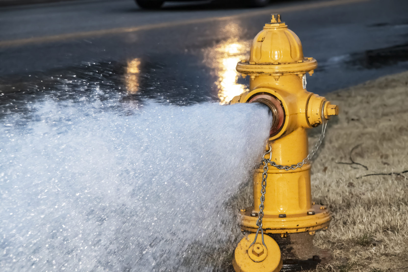 A yellow hydrant gushes water across the street. LCA crews open hydrants to perform system flushing.