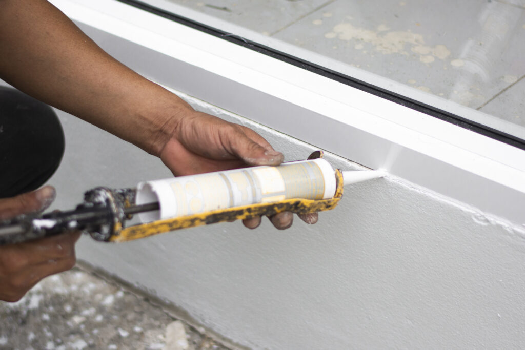 A picture of a person caulking around a window, for an LCA post on winterizing your home and avoiding frozen pipes and meters. 