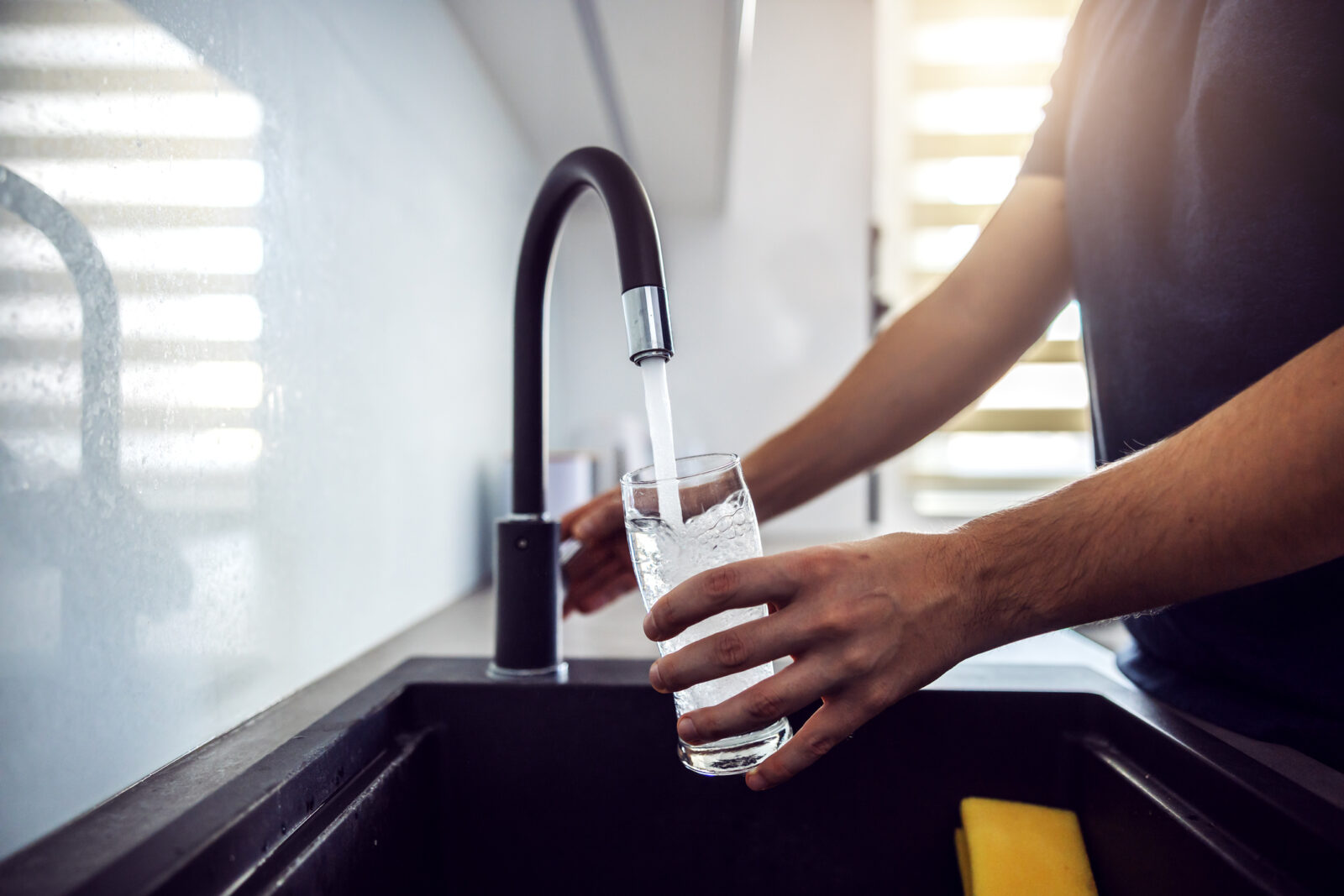 A closeup picture of a man using a sink to fill a glass with water, to illustrate an LCA blog post on the new infrastructure bill.