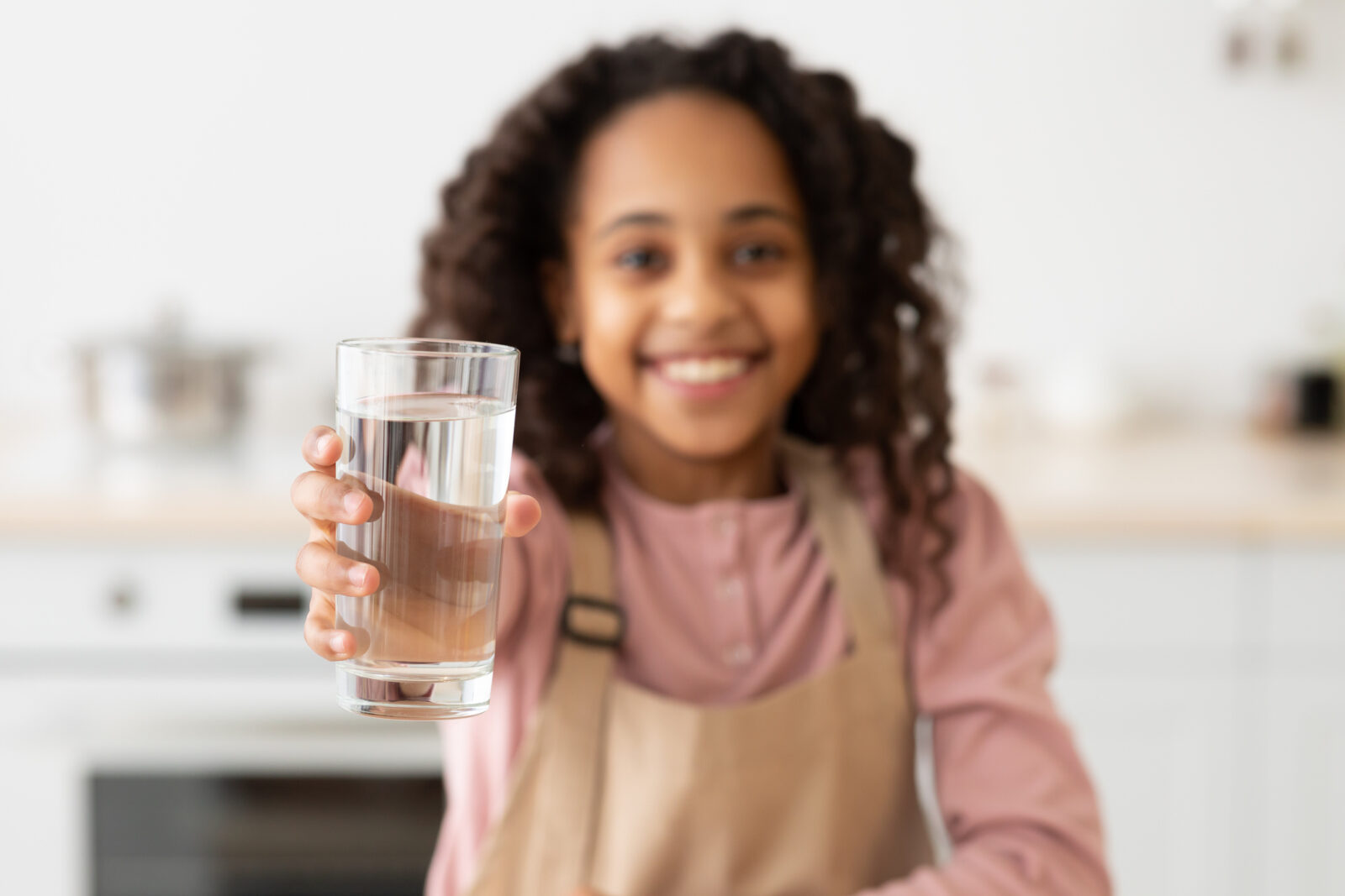 A picture of a young African American girl holding out a glass of water, for a LCA post on drinking water week.