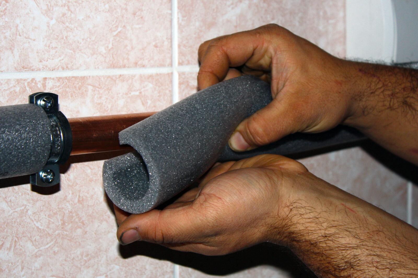 A picture of someone fitting foam insulation over a water pipe to protect it from freezing, to illustrate an LCA blog post on protecting pipes and water meters.