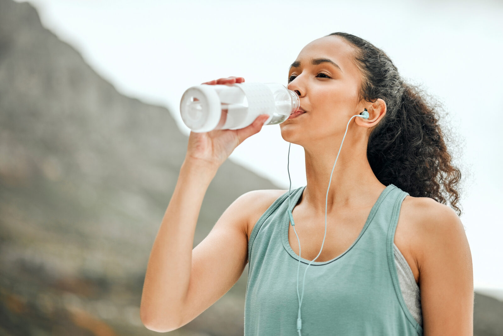 A picture of a young woman with dark hair drinking water after exercising, to illustrate an LCA blog post on Drinking Water Week 2023.