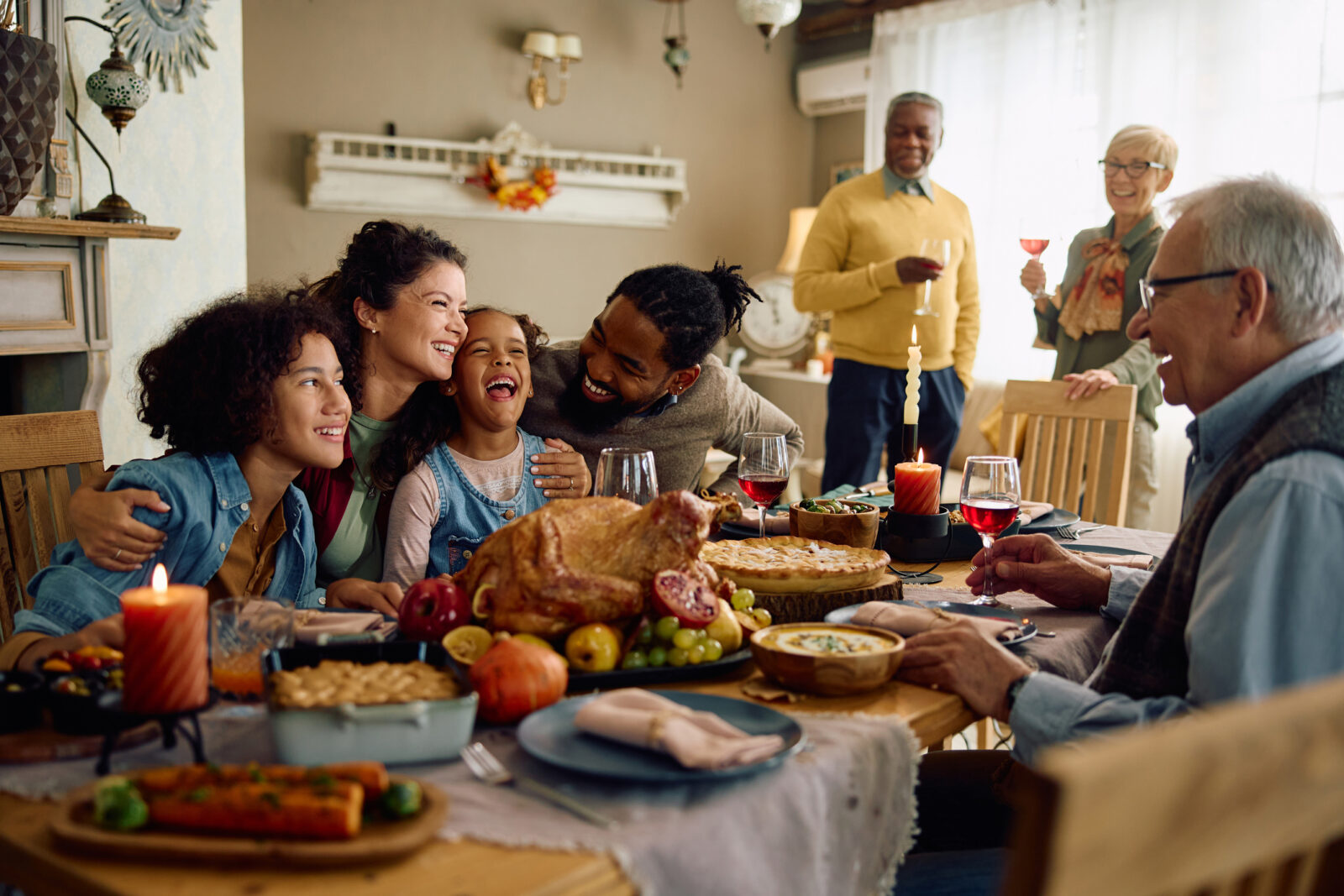A multiracial family gathers for Thanksgiving dinner around the table. When they made dinner, they poured off grease and fat into cans, froze it, and disposed of it in the trash. Pouring fats, oils and grease (FOGs) down the drain causes expensive clogs.