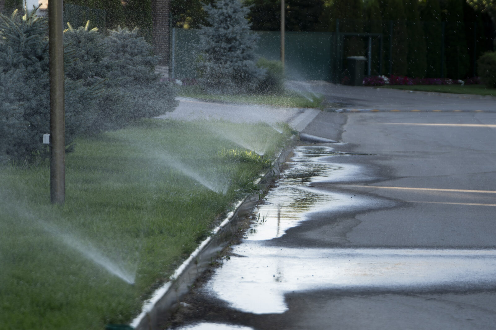 A misaligned water sprinkler system sprays the street, wasting water.